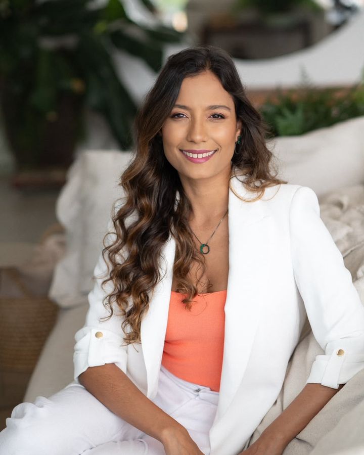 Dra. Bárbara Costa Lemos, ginecologista, sentada e sorrindo, de blazer branco.